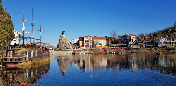 Buildings by river against clear blue sky