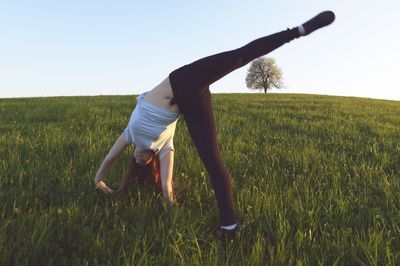 Full length of girl doing handstand on field against clear sky