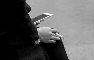 Rear view of man smoking cigarette while using smart phone