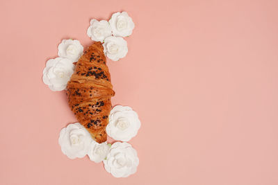 Freshly baked croissant with chocolate and white paper flowers on pink background