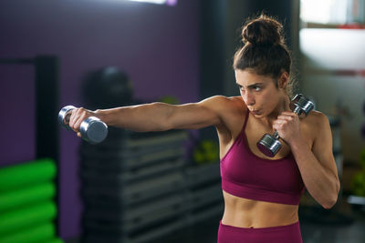 Young woman holding dumbbells while exercising in gym