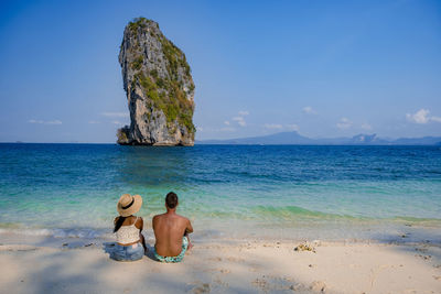 Rear view of couple relaxing on beach against sky