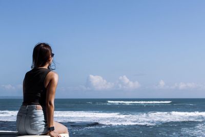 Rear view of woman sitting at beach against sky