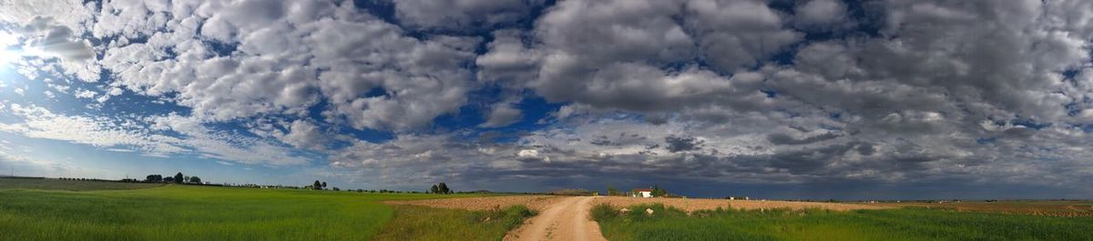 Panoramic view of road amidst field against sky