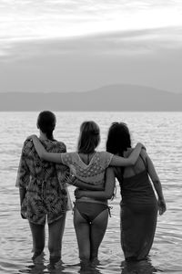 Rear view of female friends standing in sea against sky