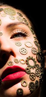 Close-up of young woman with gears on face against black background