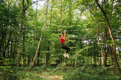Woman hanging on rope while zip lining in forest