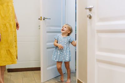 A little playful daughter plays hide and seek with her mother outside the door of the room.