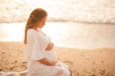 Side view of woman sitting on sand at beach