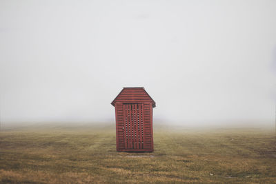 Wooden cabin on grassy filed against sky during foggy weather