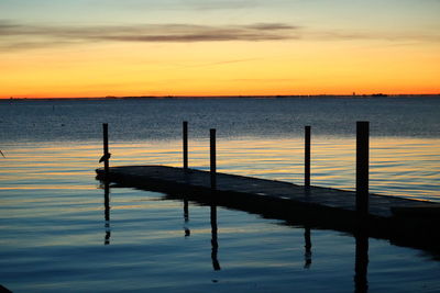 Wooden posts in lake against sky during sunset