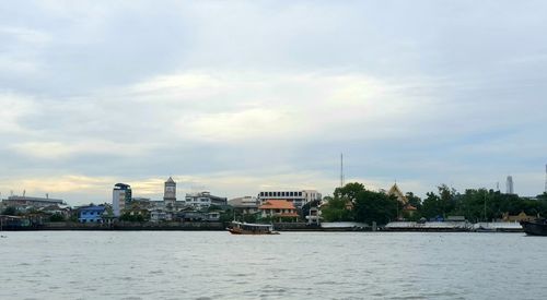 Buildings at waterfront against cloudy sky