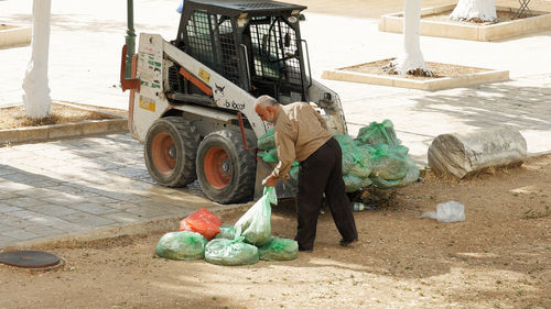 Full length of worker holding plastic bag by forklift on field