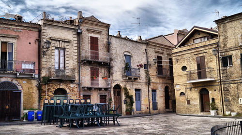 Empty chairs and tables in street by buildings against sky