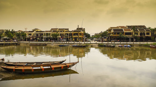 Boats moored in lake by buildings against sky