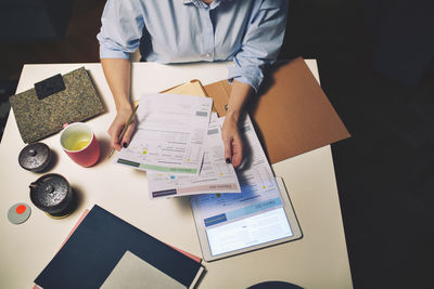 Midsection of businesswoman holding documents while sitting at desk in home office