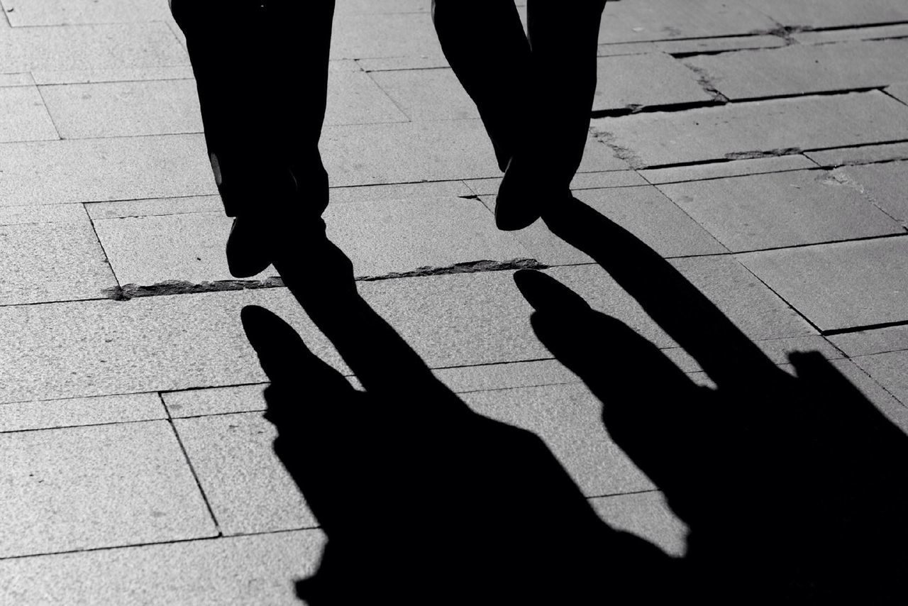 LOW SECTION OF SILHOUETTE PEOPLE WALKING ON TILED FLOOR