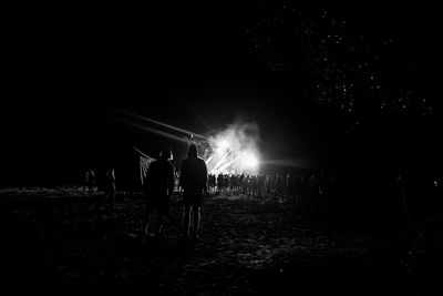 Rear view of people standing on field at night