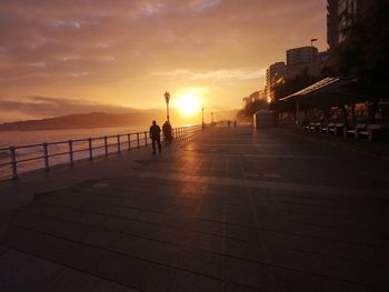 People on footpath by sea against sky during sunset