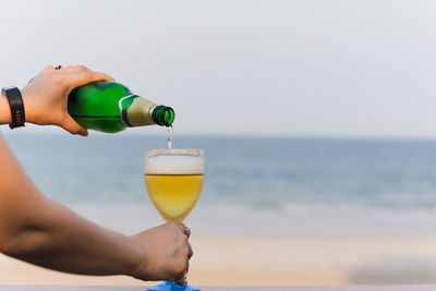 Woman hand pouring beer in glass on the beach
