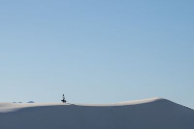 Young woman with dog walking on snow covered hill clear blue sky