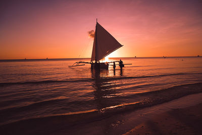 Silhouette sailboat on beach against sky during sunset