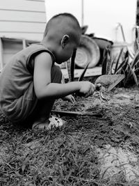 Side view of boy holding trowel while crouching on field