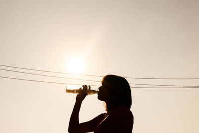 Side view of silhouette woman drinking against clear sky during sunset