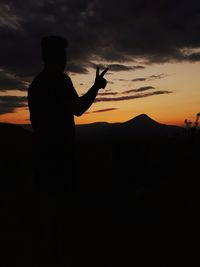 Silhouette man with arms raised standing against sky during sunset