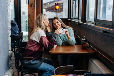 Two young attractive women are chatting and drinking coffee while sitting in a cozy bar in winter.