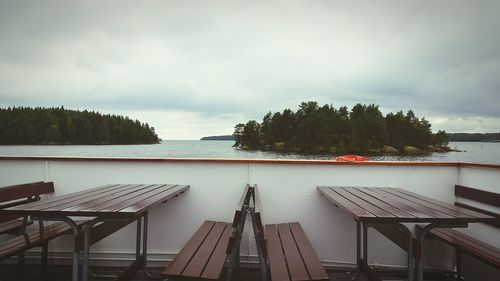 Benches and tables in ferry boat over lake against sky