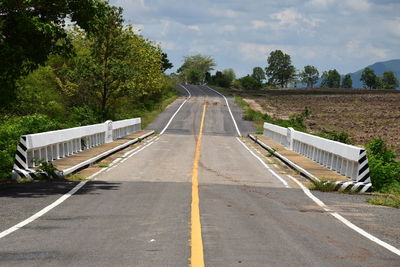 Empty road by trees against sky