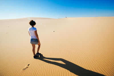 Rear view of woman walking on sand against clear sky at desert during sunny day