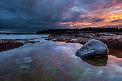 Reflection of rocks in lake against sky during sunset