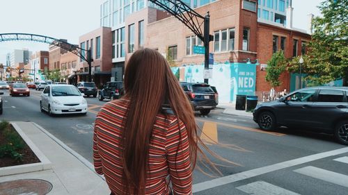 Rear view of woman on road by buildings in city