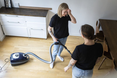 High angle view of young lesbian woman talking to girlfriend while standing with vacuum cleaner at home