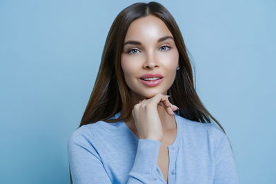 Portrait of young woman standing against blue background