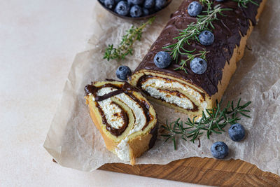 Sponge cake roll with chocolate and cream cheese decorated with glaze, blueberry and rosemary.