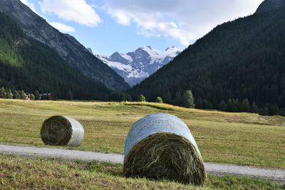 Hay bales on field by mountains against sky