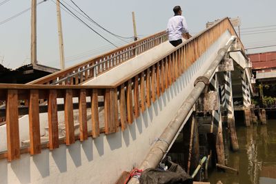 Rear view of man walking on footbridge against clear sky