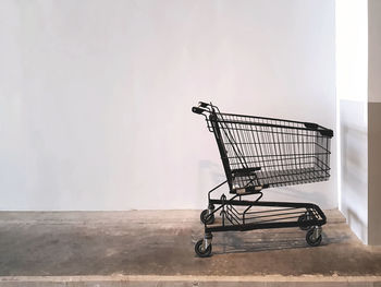 Close-up of empty shopping cart on floor against white wall