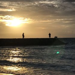 Silhouette people standing on sea against sky during sunset