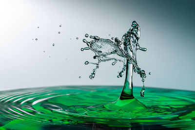 Close-up of drop falling on glass against white background