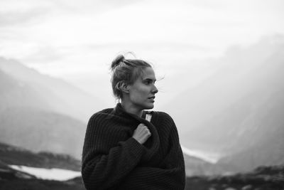 Portrait of young woman looking at mountains against sky