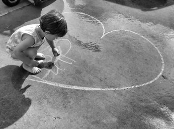 High angle view of boy drawing heart shape on footpath