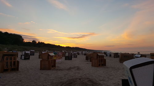 Hooded chairs on beach against sky during sunset