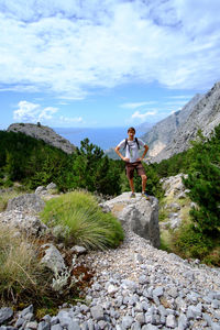 Young woman standing on rock against sky