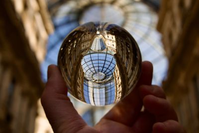 Close-up of hand holding crystal ball against glass ceiling 