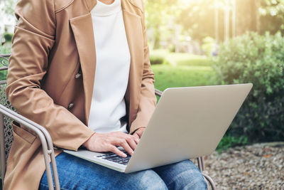 Midsection of woman using laptop while sitting on chair