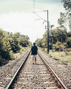 Rear view of man walking on railroad track